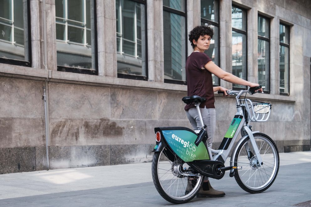 Frau steht neben ihrem Euregiobike Leihrad und dreh sich zur Kamera um