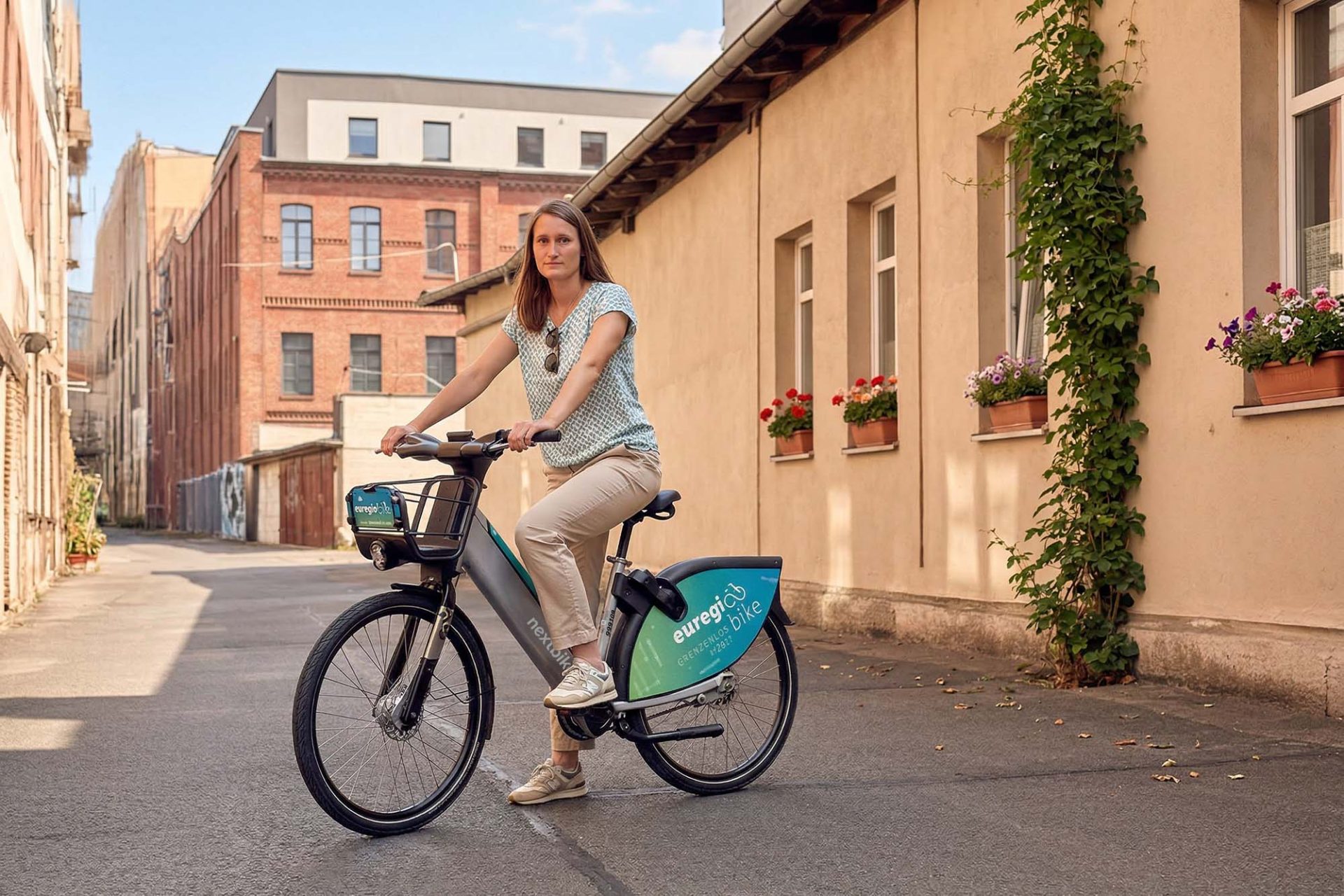 Junge Frau sitzt auf dem Sattel ihres euregiobike Leihrads neben einer Hauswand